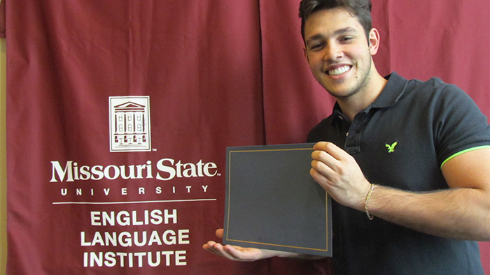 Student holding a diploma in front of MSU EAP banner.