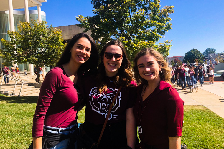 Three students on campus in Bear wear.