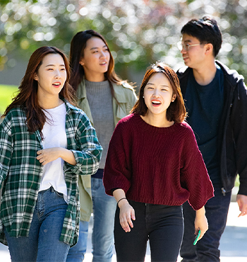 Four individuals walk outdoors together along a campus pathway in a casual setting. 