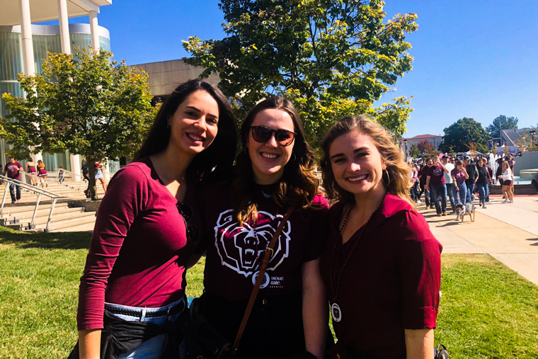 Three women in maroon attire, including a Missouri State Bears t-shirt, smiling on a sunny campus. 