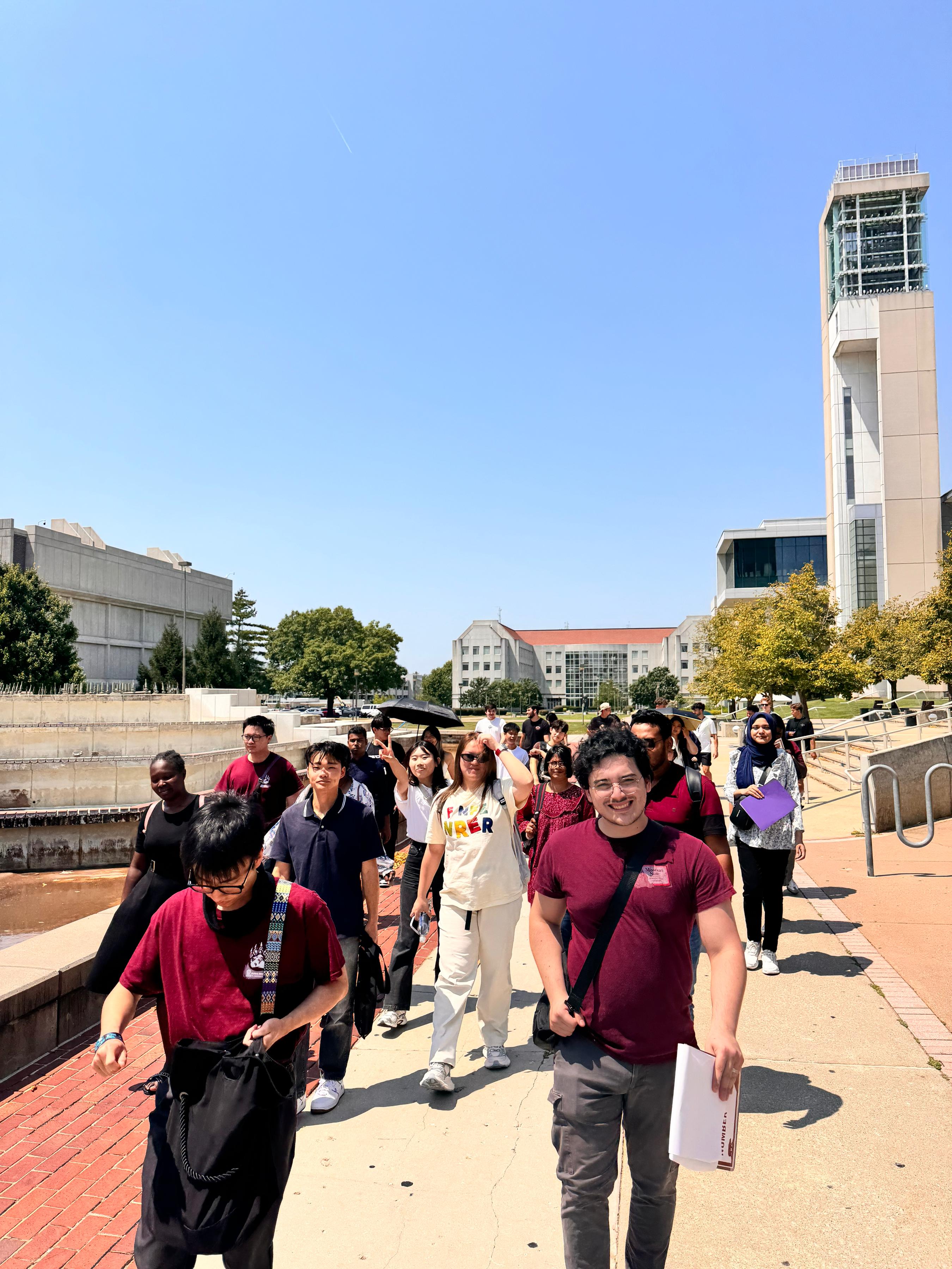 International students walking across campus with a mentor on a sunny day, exploring university facilities and student life.